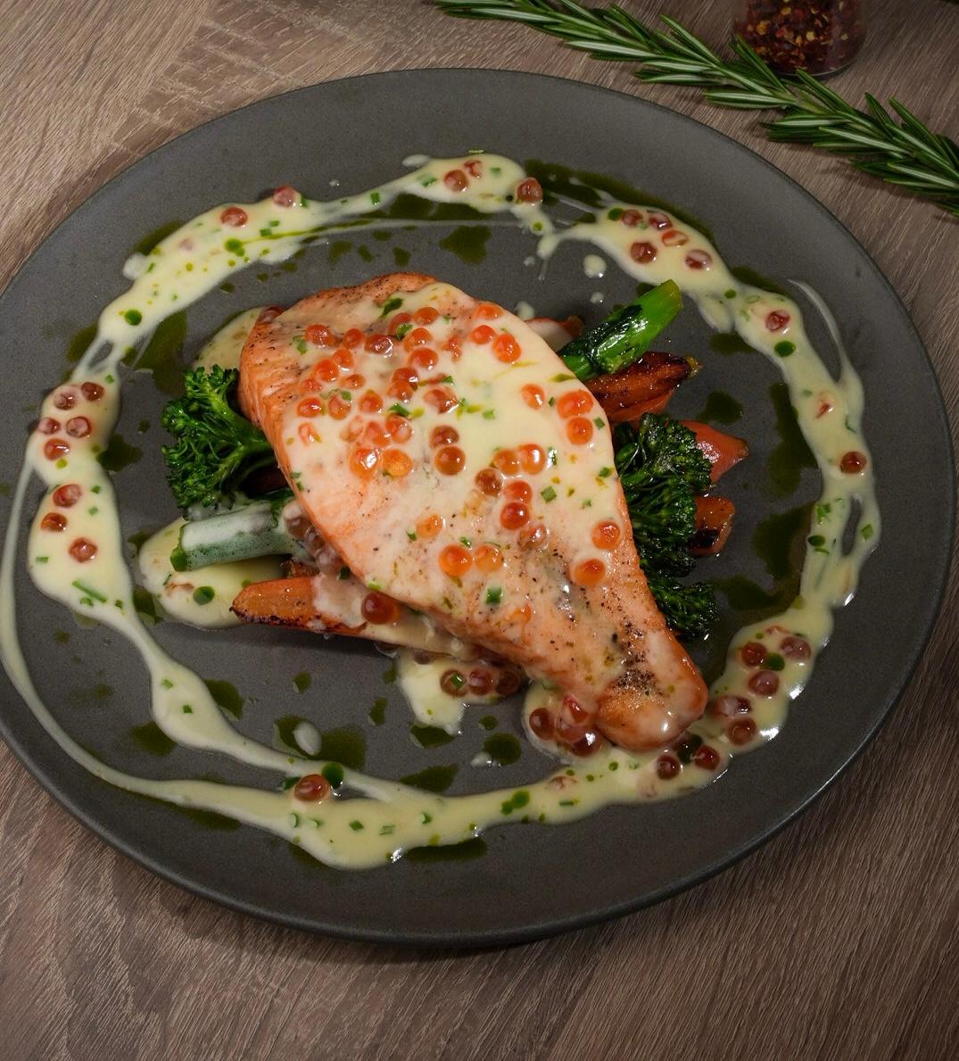 Salmon steak with creamy sauce, red caviar, broccolini and carrots.